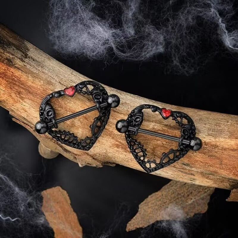 Gothic style nipple barbells displayed on a wooden branch with spooky decor.