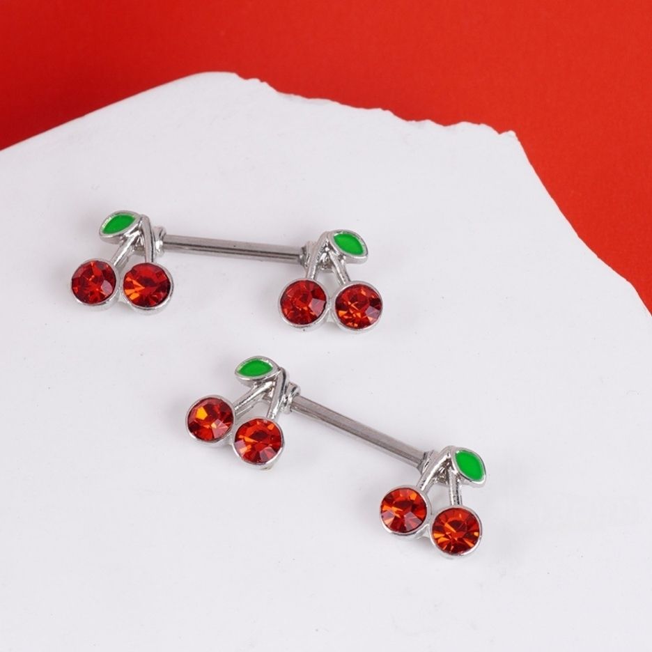Red cherry nipple piercings displayed on a white textured surface.
