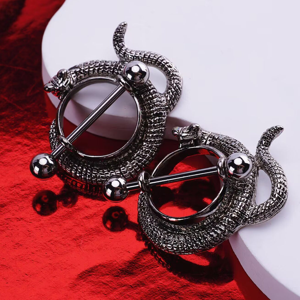 A pair of antique finish serpent nipple shields resting on a white and red background
