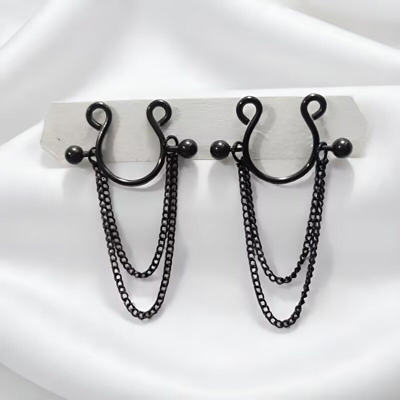 A pair of sleek black minimalist goth faux nipple rings featuring layered dangle chains on a white satin background.