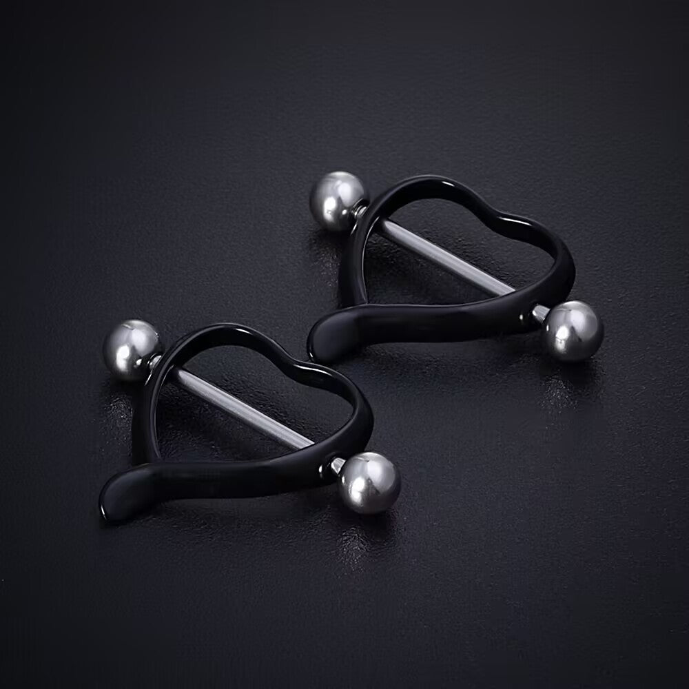 Pair of matte black heart nipple shields on dark surface