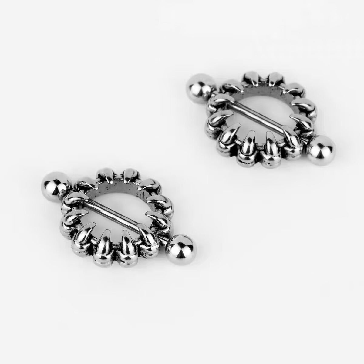 Two claw-design nipple shields shown at an angle, highlighting the interlocking fang details and the barbell.