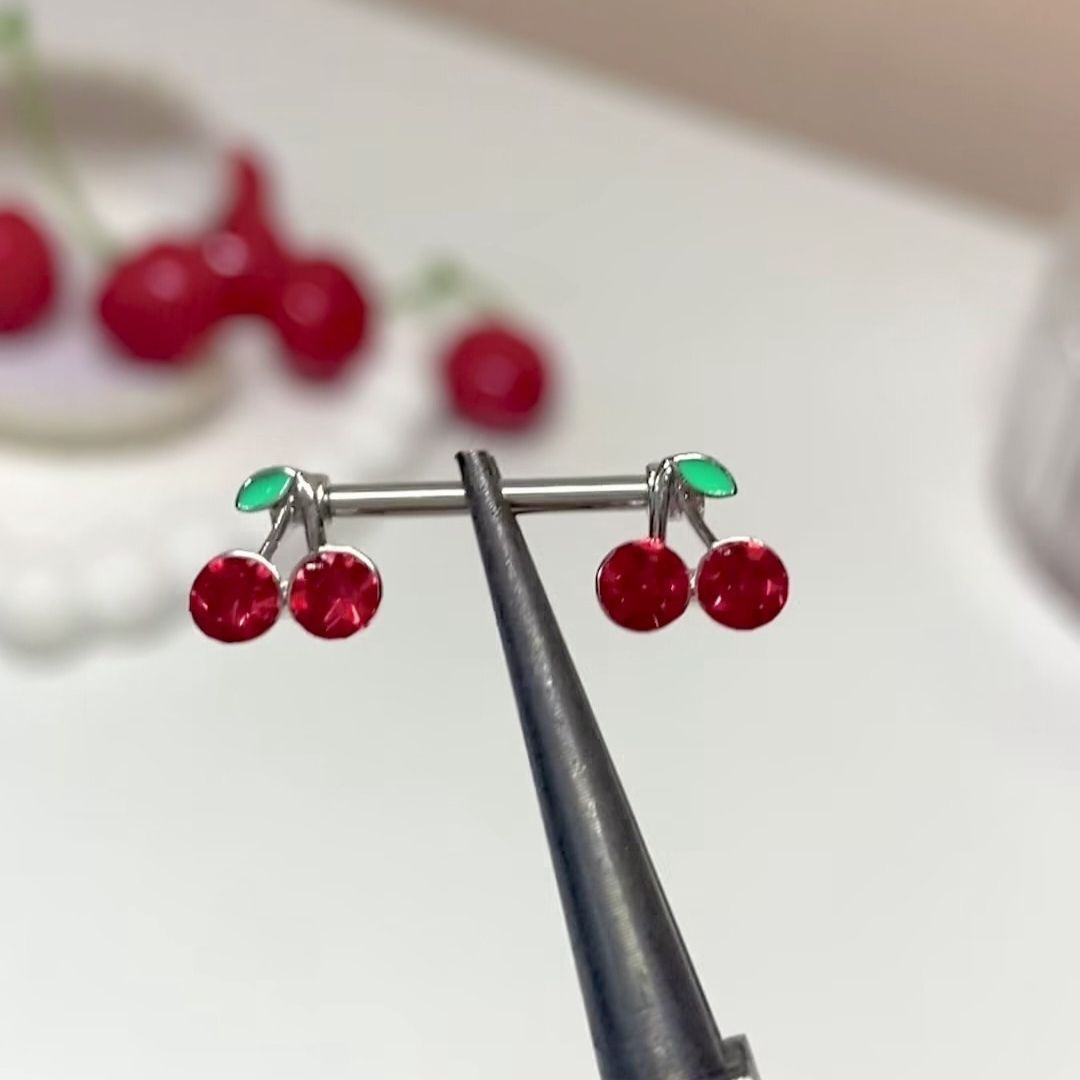 Close-up shot of a red cherry nipple barbell held with professional tools.