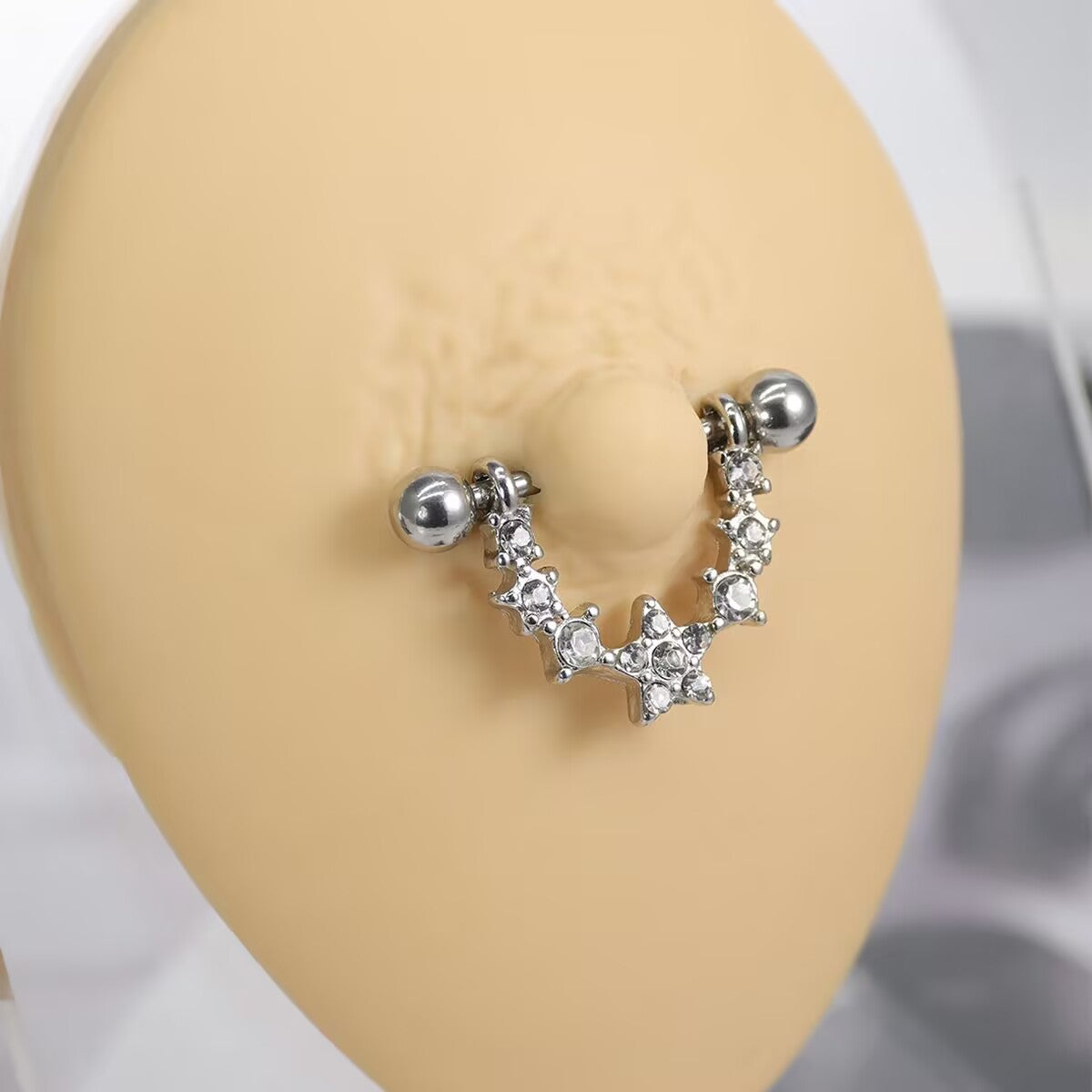 A dainty U-shaped star nipple shield barbell being worn on a piercing mannequin to show its placement and look.