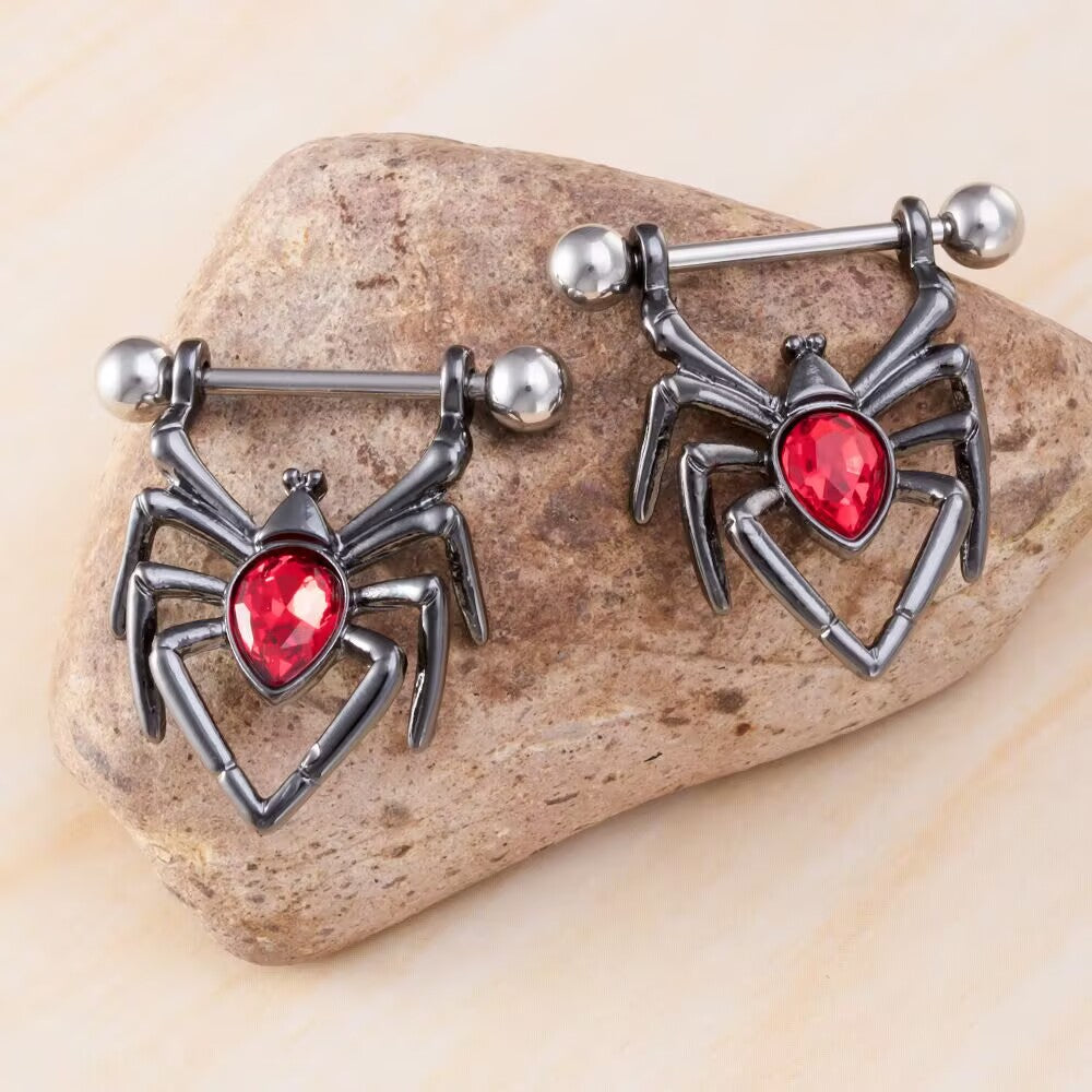 Two dark gunmetal black spider nipple shield rings with red crystals displayed on a stone.