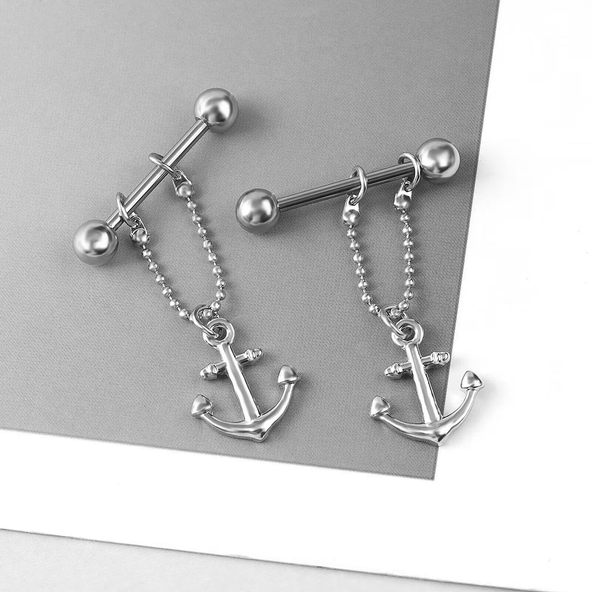 Two anchor dangle nipple barbells displayed on a stylish grey and white background