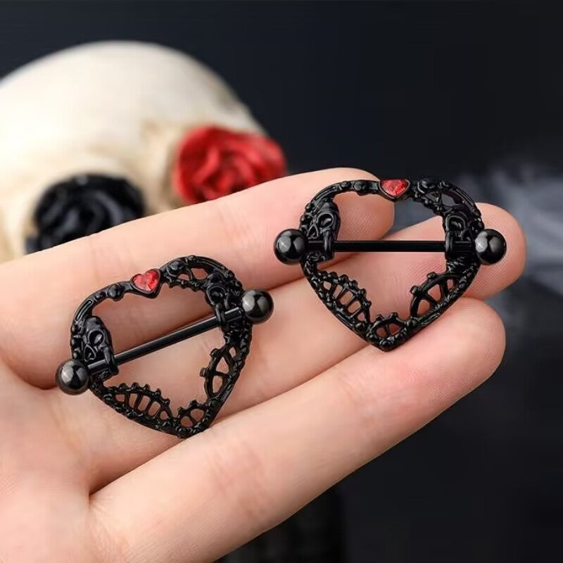 Close up of two black heart skull nipple shields held in a hand for scale.