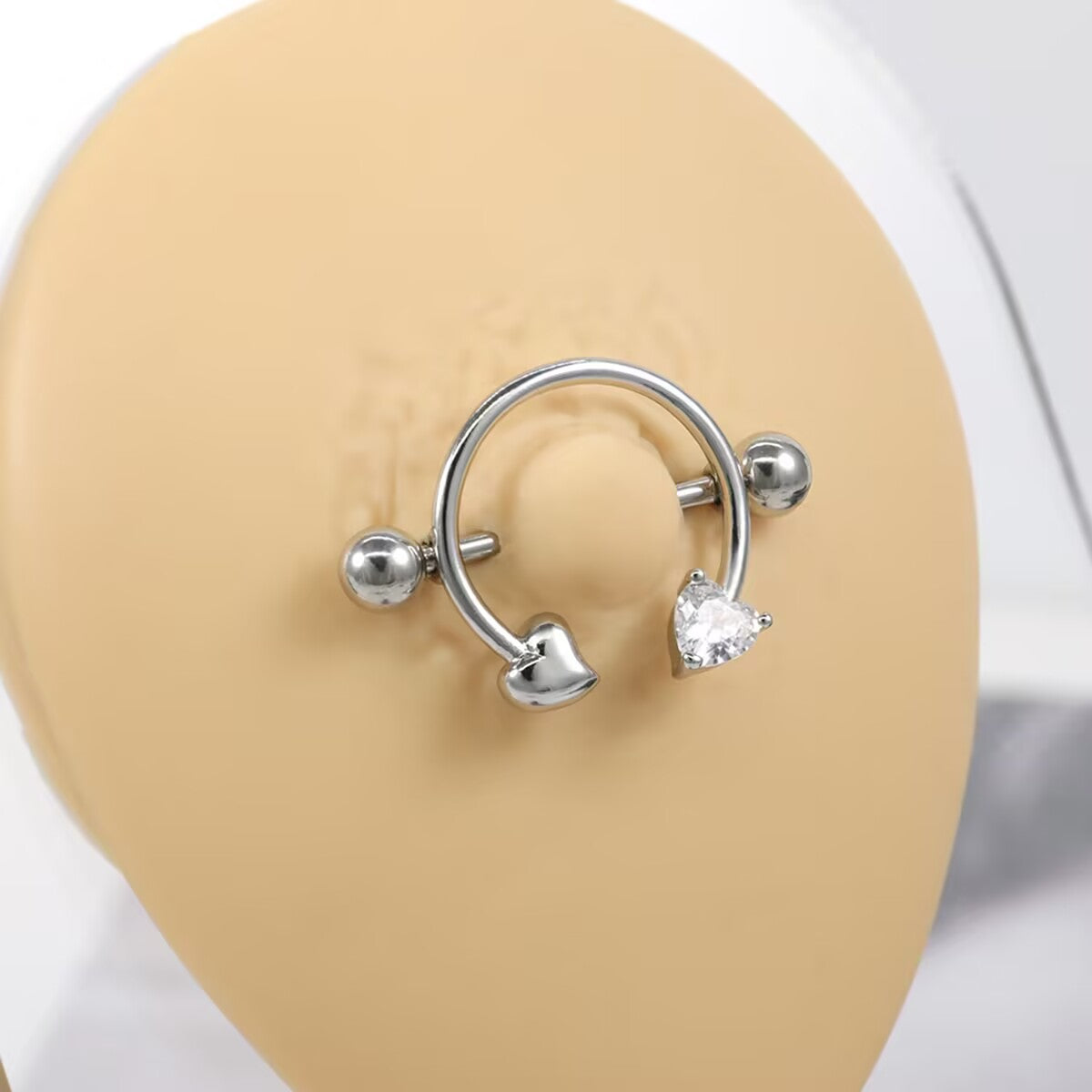 Close-up of heart nipple shield jewelry worn on a skin-tone silicone display model for size reference.